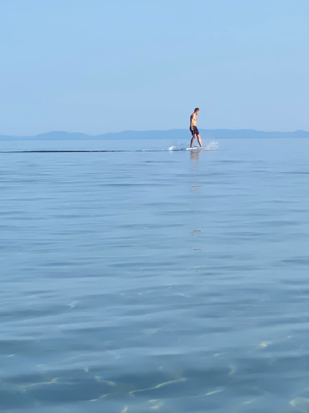 Foiling across glass-calm water at dusk with mountains in the distance